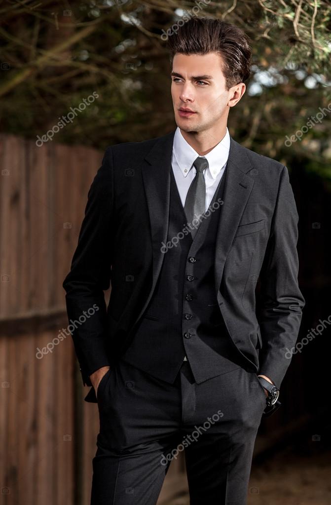 Man half face young handsome elegant model in unbutton suit with skinny  necktie poses with hand in trouser pocket holds arm sideward outdoor black  and white on masonry background Stock Photo |