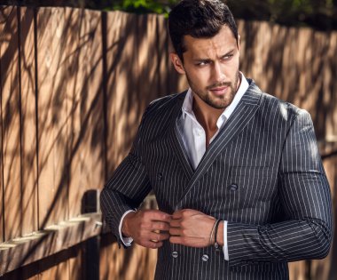 Klasik gri takım elbise teşkil ahşap çit yakınındaki zarif yakışıklı adam