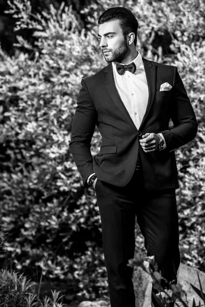Eleganter gutaussehender Mann in klassischem Kostüm posiert im Freien. Schwarz-Weiß-Foto — Stockfoto