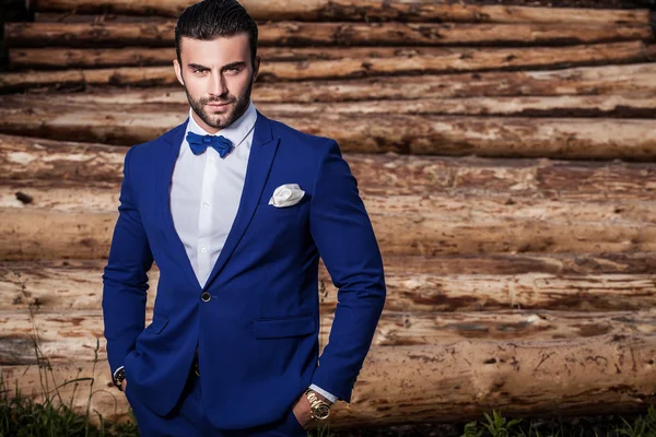 Ritratto all'aperto di giovane bello uomo alla moda contro tronchi di legno come sfondo — Foto Stock