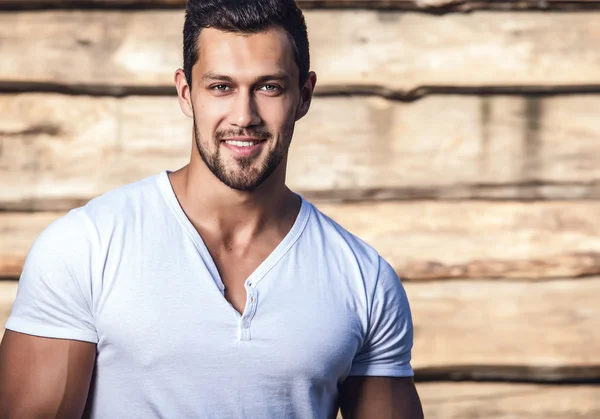 Portrait of young beautiful sporty man in t-shirt against wooden wall — Stock Photo, Image