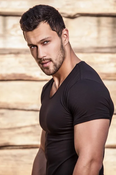 Retrato de joven hermoso hombre deportivo en camiseta contra pared de madera —  Fotos de Stock