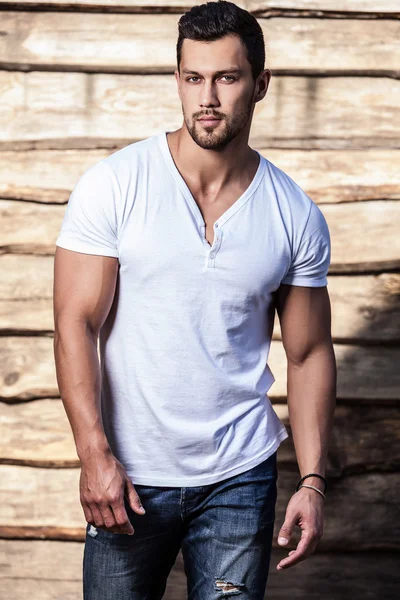 Portrait of young beautiful sporty man in t-shirt against wooden wall — Stock Photo, Image