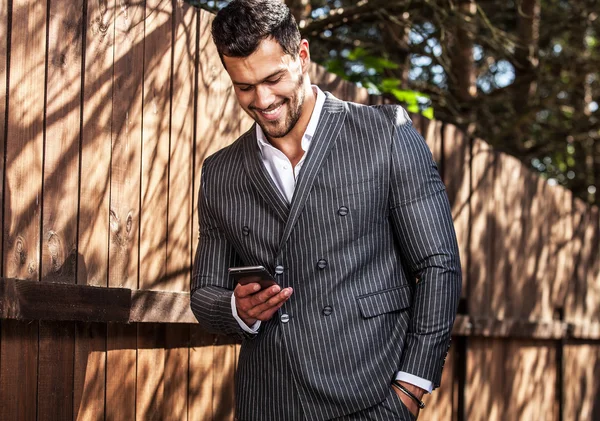 Elegante knappe man in klassieke grijs pak met zich meebrengt in de buurt van houten hek — Stockfoto