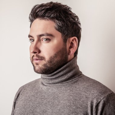 Gri süveterli zarif genç yakışıklı adam. Studio moda portre.