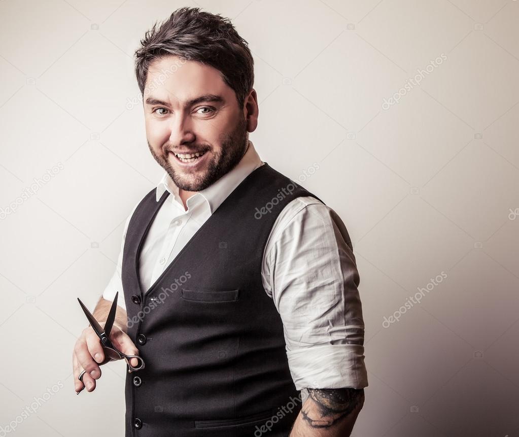 Elegant young handsome hairdresser with scissors in hand. Studio fashion portrait.
