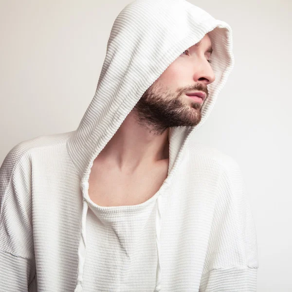 Studioporträt eines jungen gutaussehenden Mannes in weißem Pullover mit Kapuze. — Stockfoto