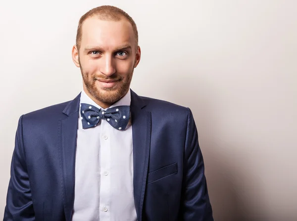 Eleganter junger gutaussehender Mann in dunkelblauem Kostüm & Fliege. Modeporträt im Studio. — Stockfoto