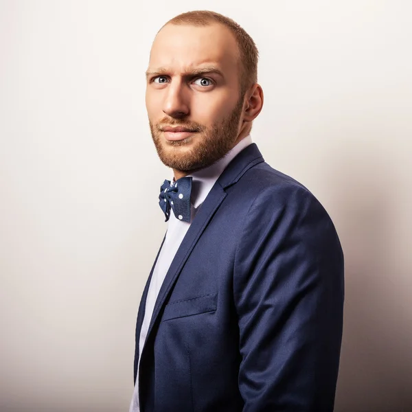 Eleganter junger gutaussehender Mann in dunkelblauem Kostüm & Fliege. Modeporträt im Studio. — Stockfoto