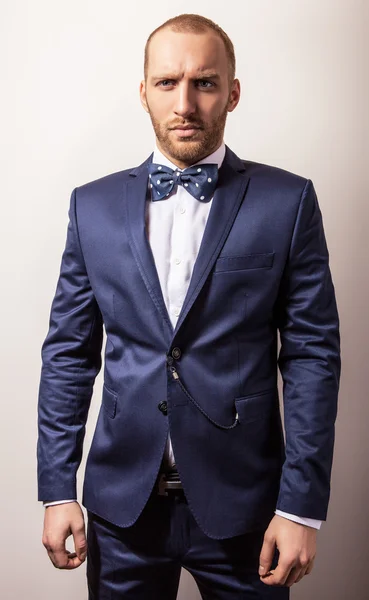 Elegant young handsome man in dark blue costume & bow tie. Studio fashion portrait.