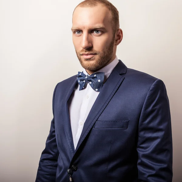 Elegant young handsome man in dark blue costume & bow tie. Studio fashion portrait. — Stock Photo, Image