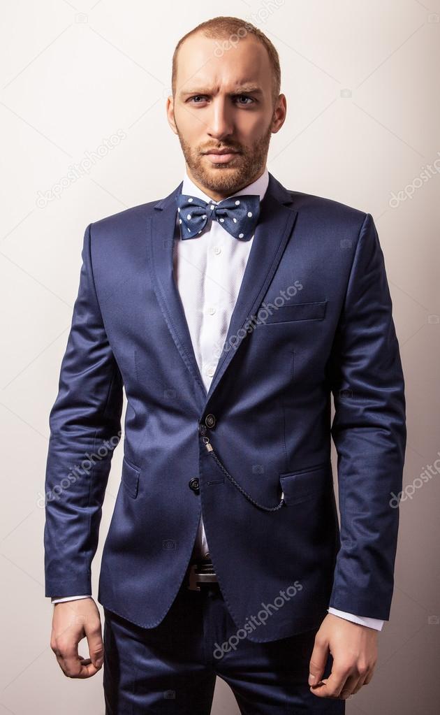 Elegant young handsome man in dark blue costume & bow tie. Studio fashion portrait.