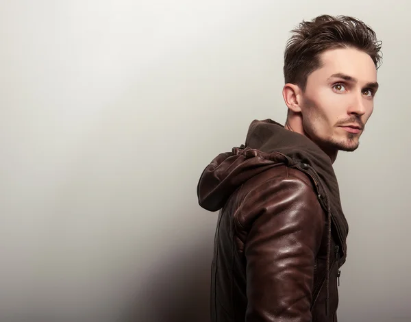 Attractive young man in a brown leather jacket pose in studio. — Stock Photo, Image