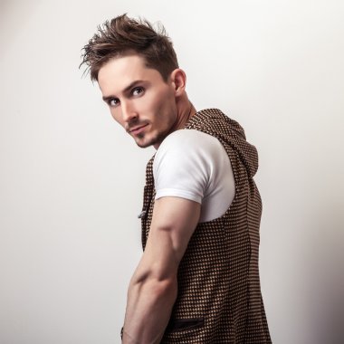 Attractive young man in a brown vest and white t-shirt pose in studio.