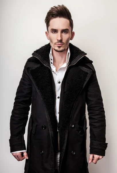 Elegante jovem homem bonito em casaco preto longo e elegante. Estúdio retrato de moda . — Fotografia de Stock