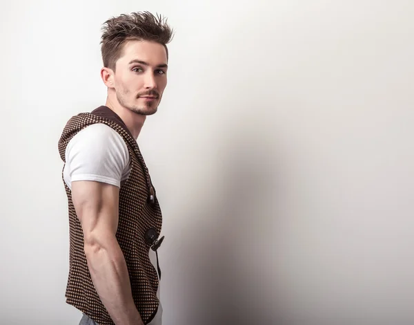 Attraente giovane uomo in un gilet marrone e bianco t-shirt posa in studio . — Foto Stock