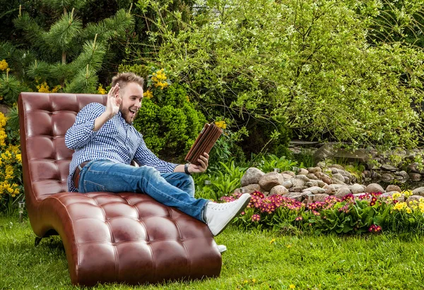 Young handsome man in casual clothes sit in luxury sofa with iPad in summer garden. — Stock Photo, Image