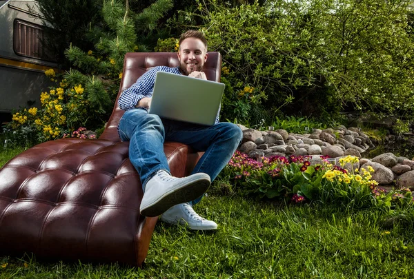 Young handsome man in casual clothes sit in luxury sofa with notebook in summer garden. — Stock Photo, Image