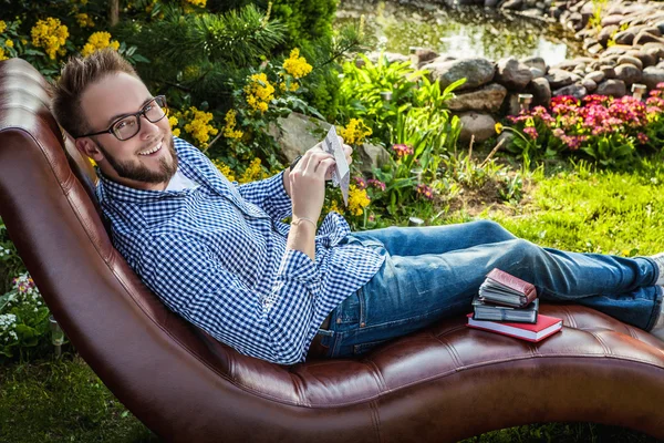 Young handsome man in casual clothes sit in luxury sofa with gift card in summer garden. — Zdjęcie stockowe