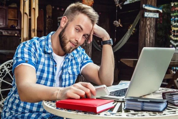 Junger lächelnder, gutaussehender Mann in lässiger Kleidung arbeitet an einem Eisentisch mit Computer gegen den Bauerngarten. — Stockfoto