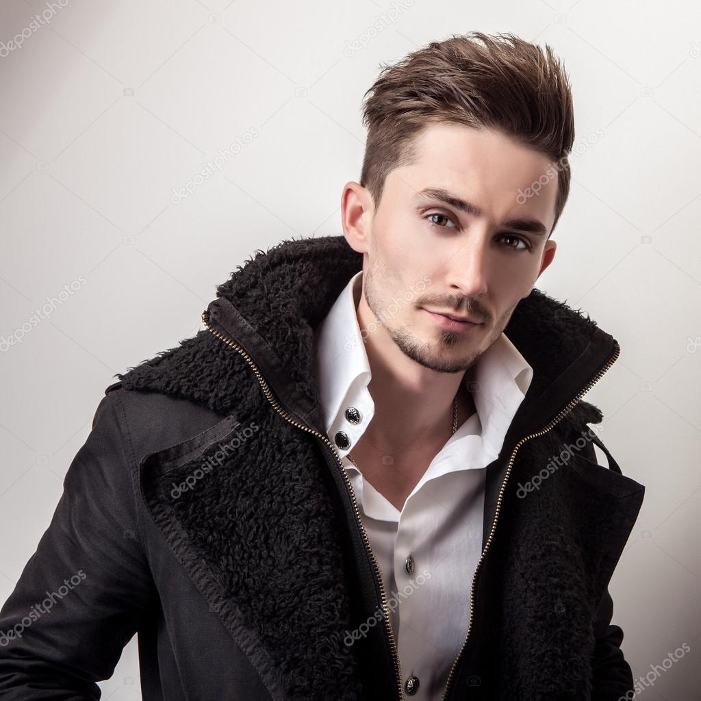 Elegant young handsome man in long stylish black coat. Studio fashion portrait.
