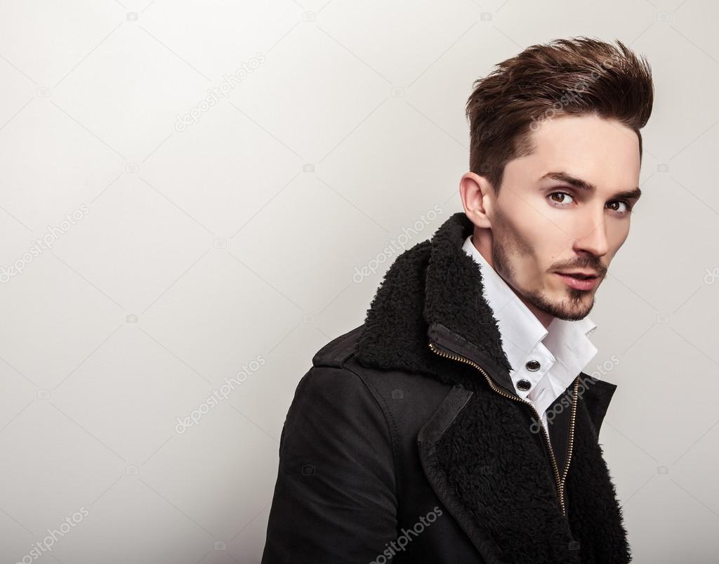 Elegant young handsome man in long stylish black coat. Studio fashion portrait.