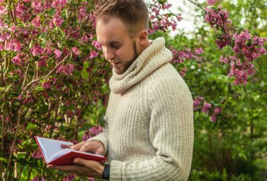 Young friendly man with red book in a summer garden at sunset.