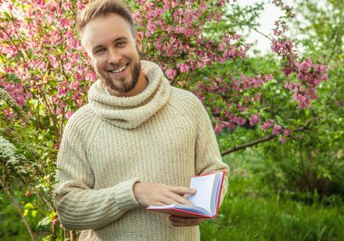Young friendly man with red book in a summer garden at sunset.