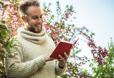 Young friendly man with red book in a summer garden at sunset.