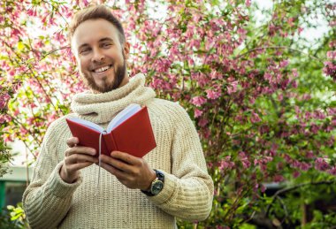 Young friendly man with red book in a summer garden at sunset.
