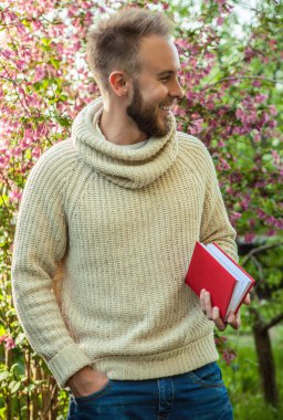 Young friendly man with red book in a summer garden at sunset.