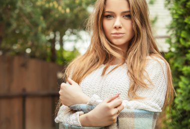 Outdoors portrait of beautiful young girl in casual white sweater & rolled in a plaid.