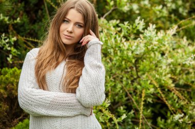 Outdoors portrait of beautiful young girl in casual white sweater.