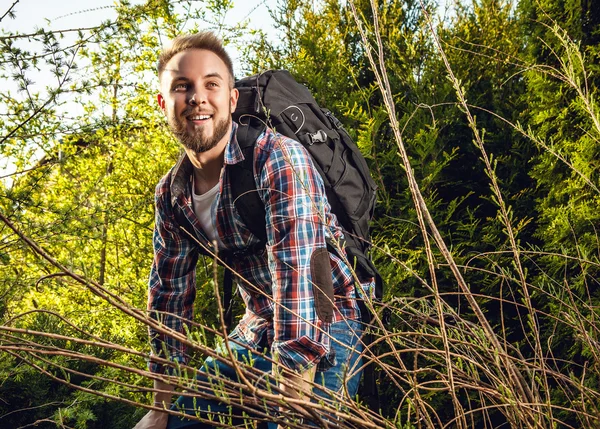 Joven hombre guapo viajero turístico con una mochila de marcha posa contra la naturaleza de verano . —  Fotos de Stock