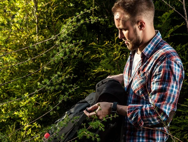 Jovem homem bonito viajante turístico com uma mochila marchando poses contra a natureza de verão . — Fotografia de Stock