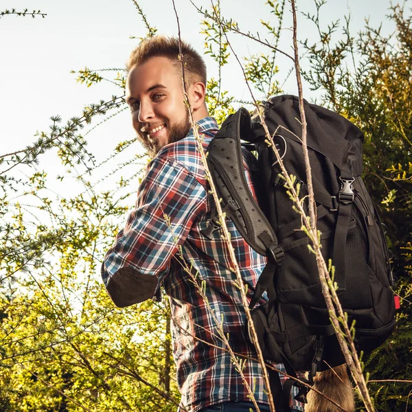 Joven hombre guapo viajero turístico con una mochila de marcha posa contra la naturaleza de verano . —  Fotos de Stock