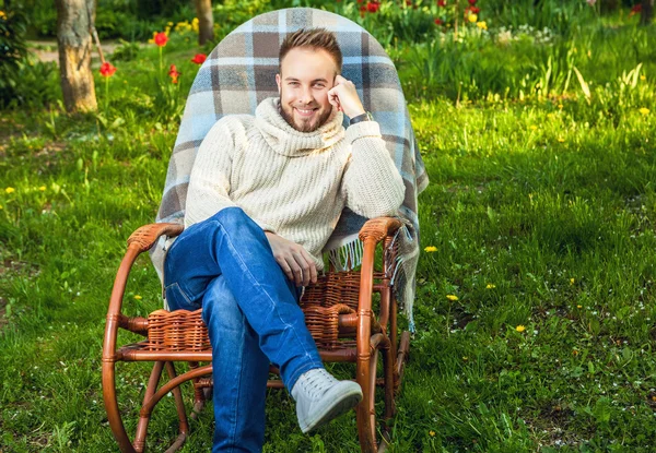 Bell'uomo rilassarsi in sedia a dondolo con plaid in un giardino estivo . — Foto Stock