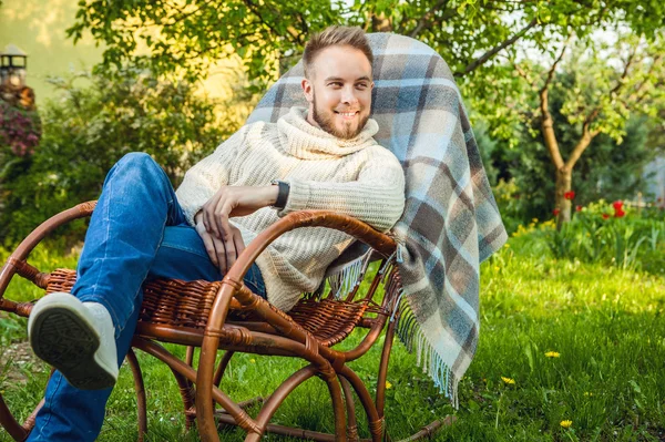 Handsome man relax in rocking-chair with plaid in a summer garden. — Stock Photo, Image