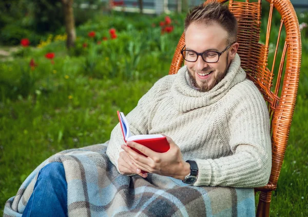 Handsome man relax in rocking-chair & reading red book in summer garden. — Stockfoto