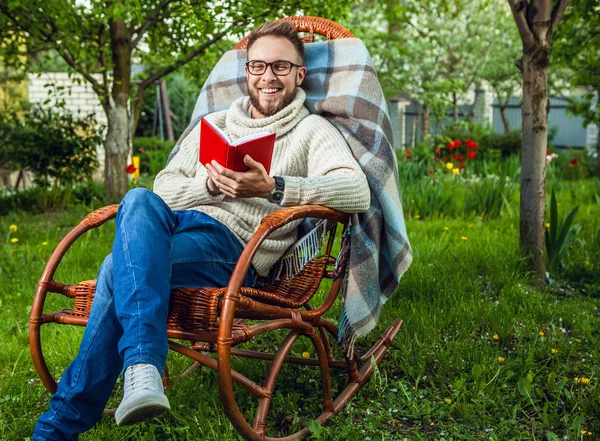 Handsome man relax in rocking-chair & reading red book in summer garden. — Stock Photo, Image