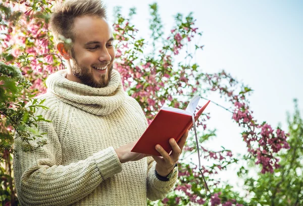 Young friendly man with red book in a summer garden at sunset.