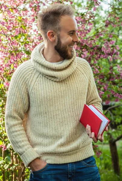 Young friendly man with red book in a summer garden at sunset. — Stockfoto