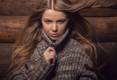 Young attractive girl in a brown sweater poses on wooden background.