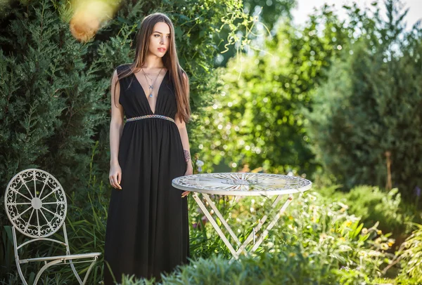 На відкритому повітрі портрет красивої молодої жінки в розкішній чорній сукні позує в літньому саду . — стокове фото