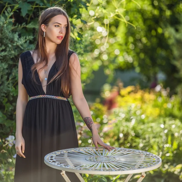 Retrato al aire libre de una hermosa mujer joven en vestido negro de lujo posando en el jardín de verano . —  Fotos de Stock