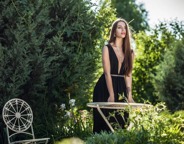 Draußen Porträt der schönen jungen Frau in luxuriösem schwarzen Kleid posiert im Sommergarten. — Stockfoto