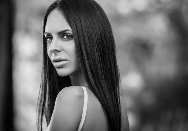 Outdoors portrait of beautiful young brunette girl in luxury dress posing in summer garden.Black-white photo.