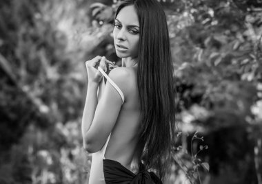 Outdoors portrait of beautiful young brunette girl in luxury dress posing in summer garden.Black-white photo.