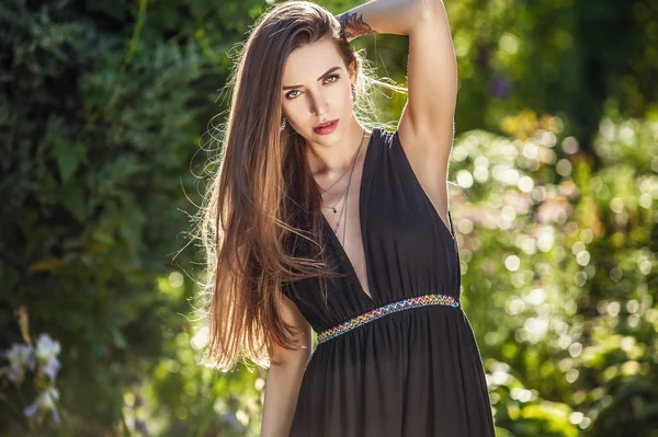 Outdoors portrait of beautiful young woman in luxury black dress posing in summer garden. — Stockfoto