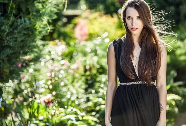 Ao ar livre retrato de bela jovem mulher em luxo vestido preto posando no jardim de verão . — Fotografia de Stock